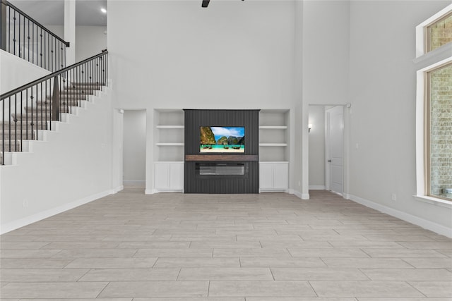 unfurnished living room with built in shelves, a towering ceiling, and light hardwood / wood-style floors