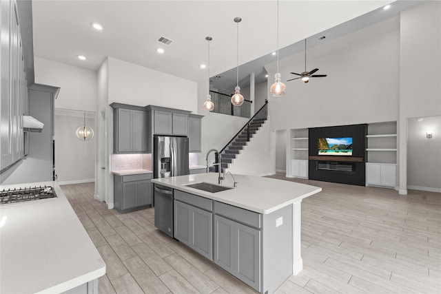 kitchen with sink, a towering ceiling, an island with sink, gray cabinets, and appliances with stainless steel finishes