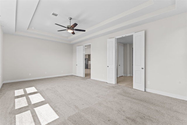 unfurnished bedroom with light carpet, a raised ceiling, and ceiling fan