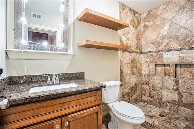 bathroom with a tile shower, vanity, and toilet