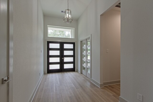 entrance foyer with a notable chandelier, light wood-type flooring, a towering ceiling, and french doors