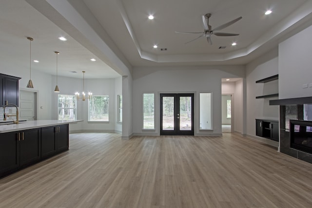 kitchen with french doors, ceiling fan with notable chandelier, hanging light fixtures, light wood-type flooring, and a fireplace