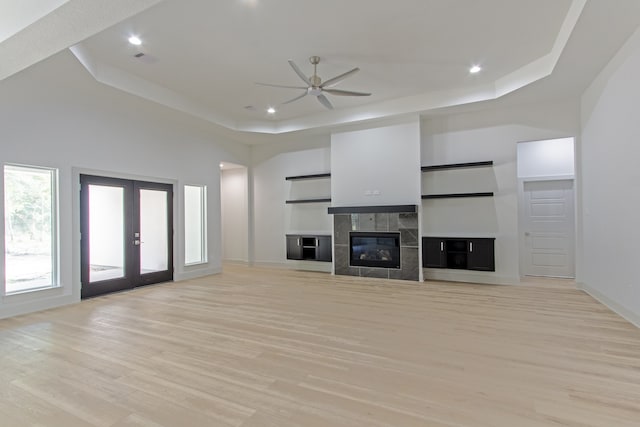 unfurnished living room with french doors, a tray ceiling, light hardwood / wood-style flooring, and ceiling fan