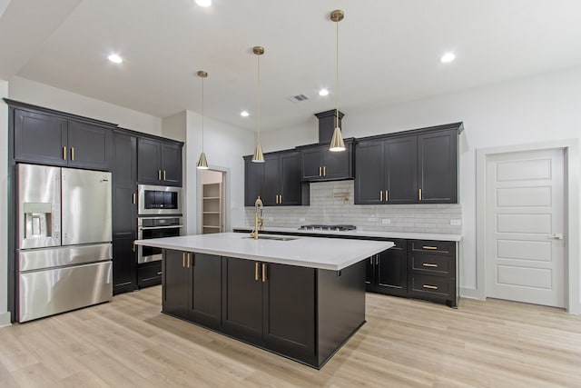 kitchen featuring stainless steel appliances, sink, light hardwood / wood-style floors, hanging light fixtures, and an island with sink