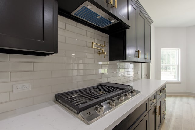 kitchen featuring tasteful backsplash, ventilation hood, light hardwood / wood-style floors, and stainless steel gas stovetop