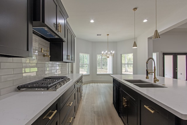 kitchen with sink, stainless steel gas cooktop, light stone counters, light hardwood / wood-style flooring, and pendant lighting