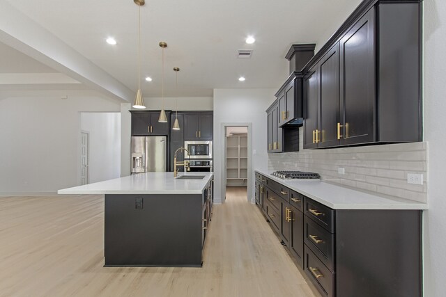 kitchen with stainless steel appliances, light hardwood / wood-style flooring, backsplash, an island with sink, and pendant lighting