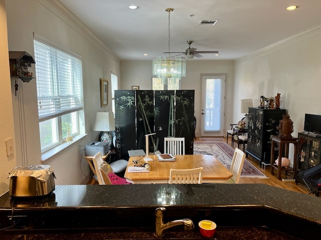 dining room with wood-type flooring, ceiling fan with notable chandelier, crown molding, and a healthy amount of sunlight