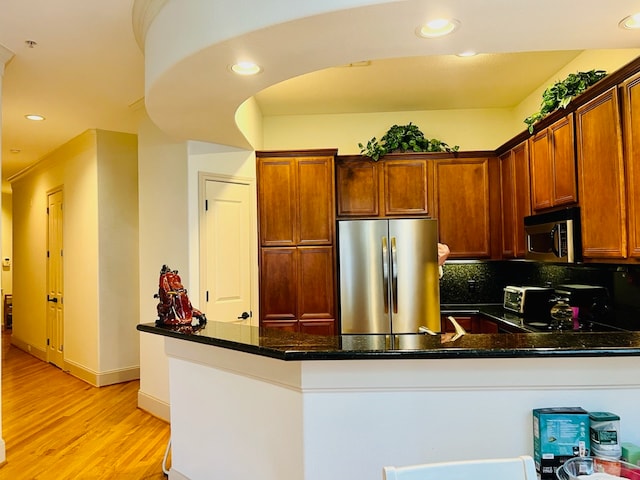 kitchen with light hardwood / wood-style floors, dark stone countertops, kitchen peninsula, and stainless steel appliances