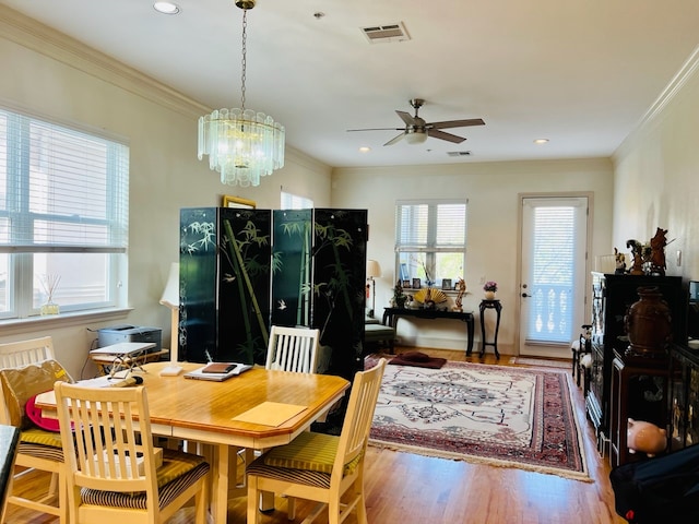 dining space featuring wood-type flooring, ceiling fan with notable chandelier, and crown molding