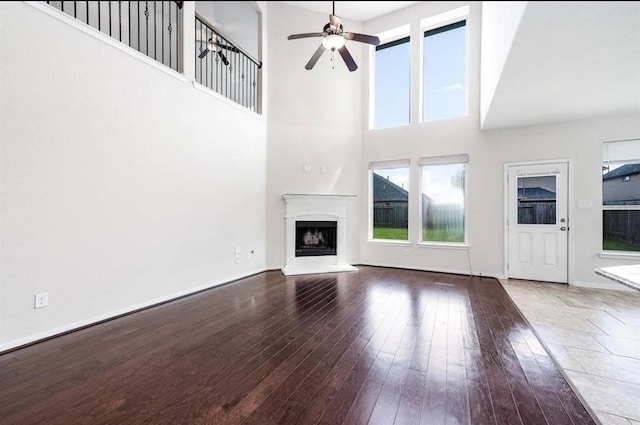 unfurnished living room with hardwood / wood-style floors, a towering ceiling, and ceiling fan