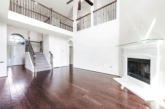 unfurnished living room featuring ceiling fan, dark hardwood / wood-style flooring, and a towering ceiling