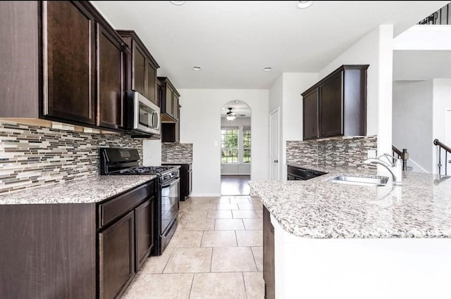 kitchen featuring backsplash, black range with gas stovetop, sink, ceiling fan, and light stone counters