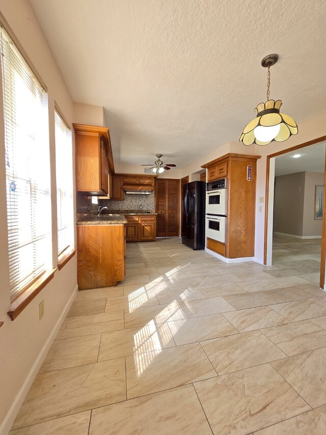 kitchen featuring black refrigerator, decorative backsplash, kitchen peninsula, double oven, and sink