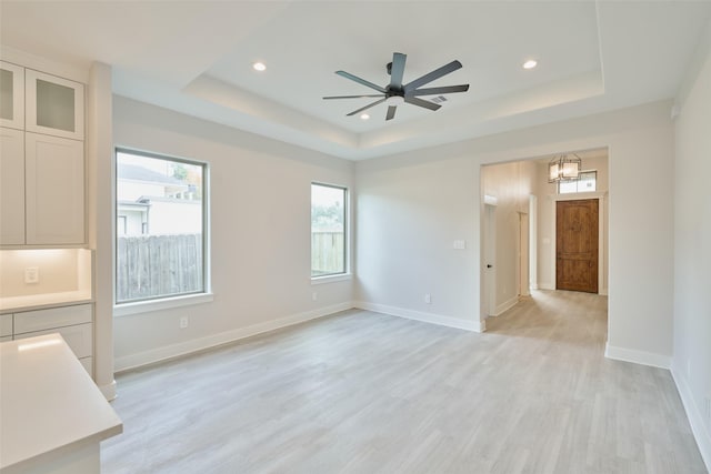 unfurnished room with a tray ceiling, light hardwood / wood-style floors, and ceiling fan with notable chandelier