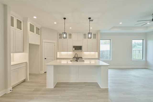 kitchen with ceiling fan, light hardwood / wood-style floors, decorative light fixtures, a kitchen island with sink, and appliances with stainless steel finishes