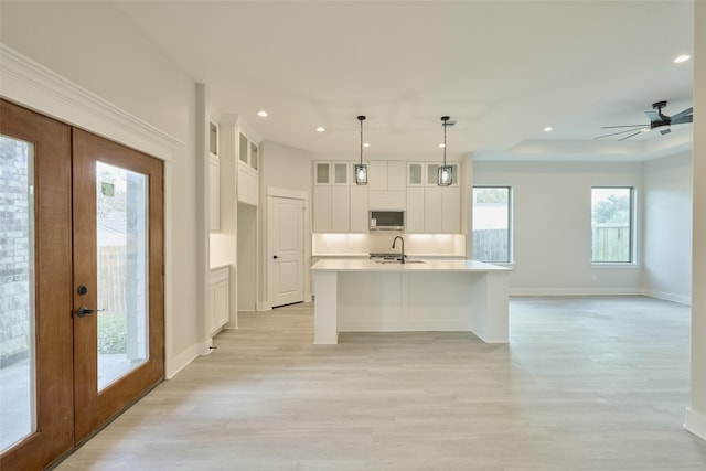 kitchen featuring french doors, a center island with sink, decorative light fixtures, and light hardwood / wood-style flooring