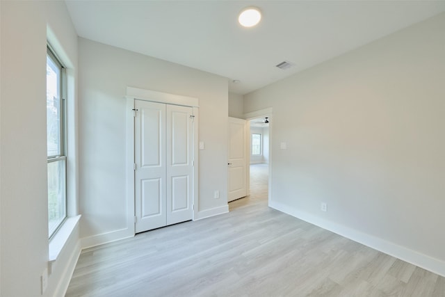 unfurnished bedroom with light wood-type flooring, a closet, and multiple windows