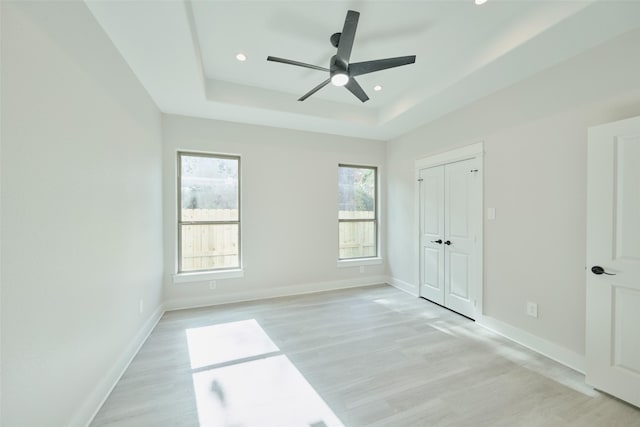 unfurnished bedroom featuring a raised ceiling, a closet, ceiling fan, and light hardwood / wood-style flooring