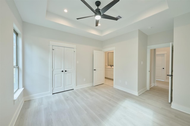 unfurnished bedroom featuring a tray ceiling, multiple windows, and ceiling fan