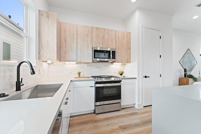 kitchen with decorative backsplash, stainless steel appliances, sink, light brown cabinets, and light hardwood / wood-style flooring