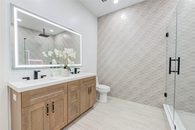 bathroom with tile patterned floors, vanity, a shower with door, tile walls, and toilet