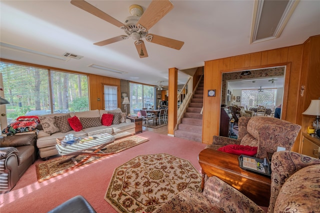 carpeted living room with ceiling fan, wood walls, and a wealth of natural light