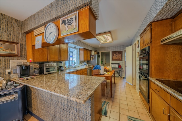 kitchen with kitchen peninsula, appliances with stainless steel finishes, light stone countertops, sink, and light tile patterned floors