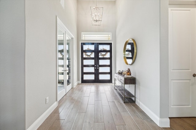 entryway with french doors, a notable chandelier, a towering ceiling, wood tiled floor, and baseboards