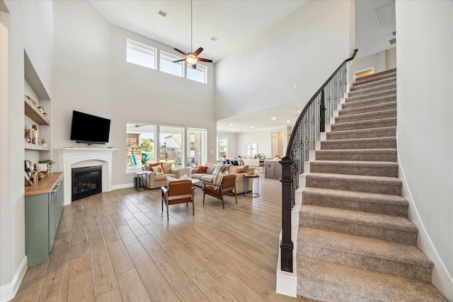 living area featuring light wood-style floors, a glass covered fireplace, a healthy amount of sunlight, and ceiling fan