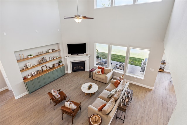 living room featuring ceiling fan, light hardwood / wood-style floors, and a towering ceiling