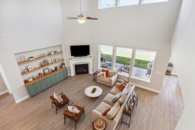 living room featuring light wood-type flooring, a fireplace, a ceiling fan, and baseboards