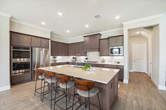 kitchen featuring sink, appliances with stainless steel finishes, a kitchen island with sink, light stone counters, and decorative backsplash