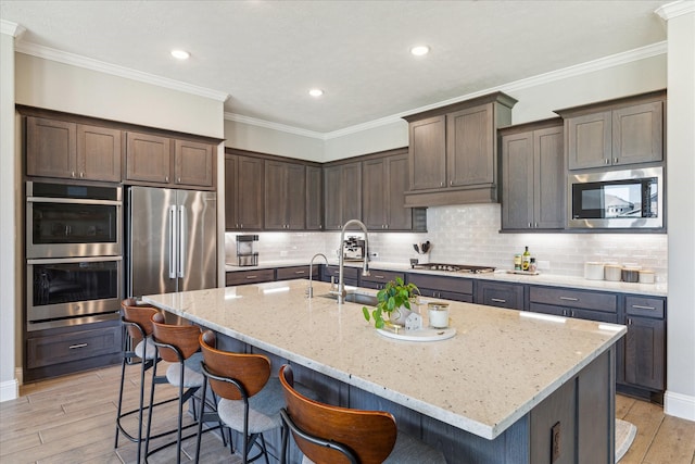 kitchen featuring light stone counters, light wood-style flooring, dark brown cabinetry, a breakfast bar, and appliances with stainless steel finishes