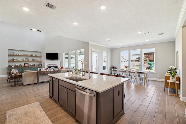 kitchen with dark brown cabinetry, sink, a center island with sink, dishwasher, and light stone countertops