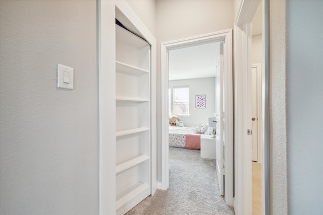 hallway featuring light colored carpet and built in features