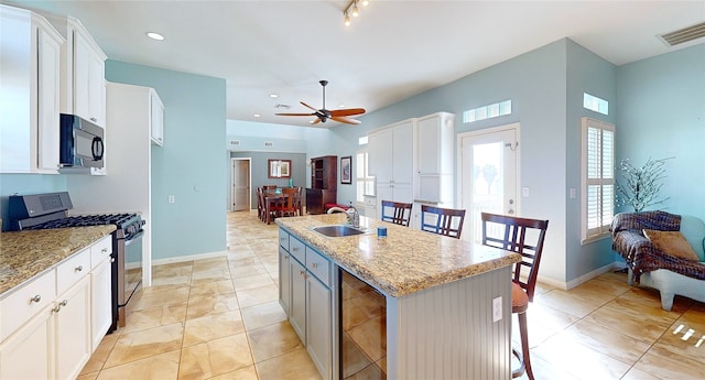 kitchen with a kitchen island with sink, stainless steel gas range, light stone countertops, and white cabinets