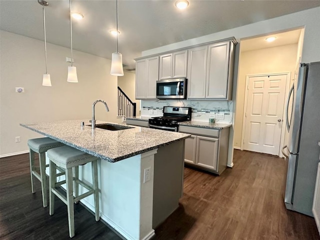 kitchen with sink, light stone counters, decorative light fixtures, a center island with sink, and appliances with stainless steel finishes