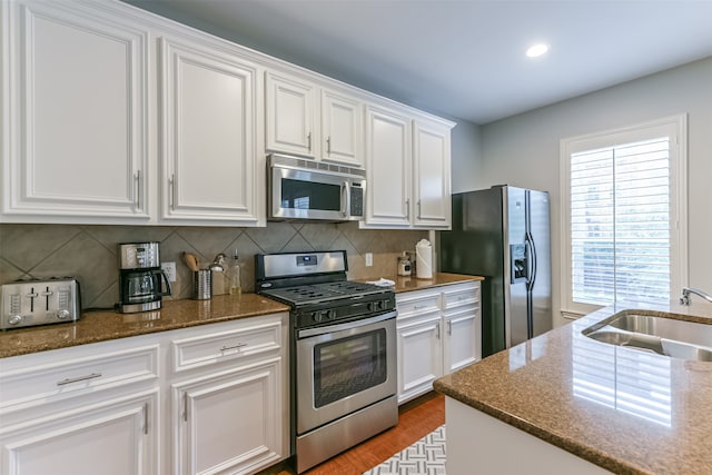 kitchen with white cabinets, appliances with stainless steel finishes, dark stone countertops, and sink