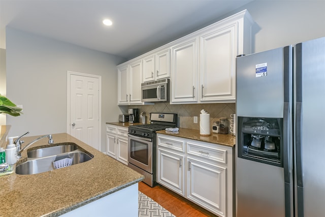 kitchen with decorative backsplash, appliances with stainless steel finishes, sink, hardwood / wood-style flooring, and white cabinetry