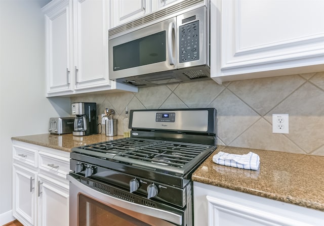 kitchen with white cabinets, stainless steel appliances, tasteful backsplash, and dark stone countertops