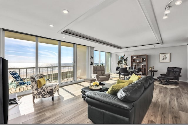 living room with a water view, floor to ceiling windows, a tray ceiling, and hardwood / wood-style flooring