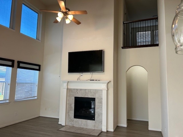 unfurnished living room featuring ceiling fan, a towering ceiling, dark wood-type flooring, and a tiled fireplace