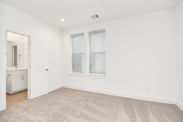 unfurnished bedroom with light carpet, ensuite bath, and sink