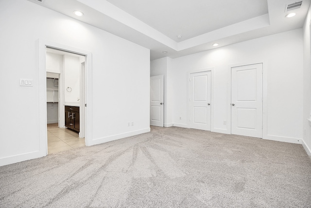 unfurnished bedroom featuring a raised ceiling, light colored carpet, and ensuite bath