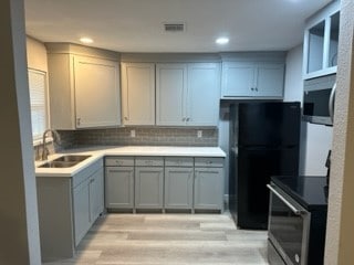 kitchen featuring appliances with stainless steel finishes, backsplash, gray cabinetry, sink, and light hardwood / wood-style floors