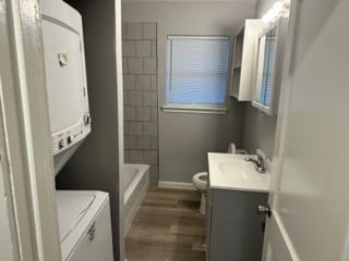 full bathroom featuring hardwood / wood-style floors,  shower combination, toilet, vanity, and stacked washer and clothes dryer