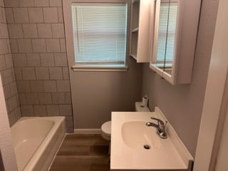 full bathroom with hardwood / wood-style flooring, tiled shower / bath combo, toilet, and sink