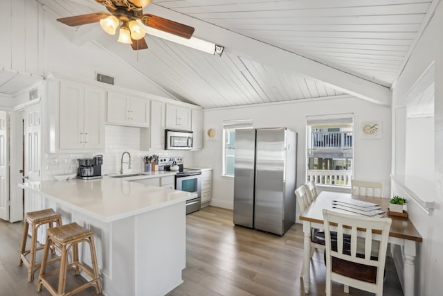 kitchen with white cabinets, sink, vaulted ceiling with beams, kitchen peninsula, and stainless steel appliances