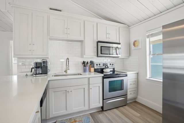 kitchen featuring appliances with stainless steel finishes, vaulted ceiling, sink, light hardwood / wood-style flooring, and white cabinets